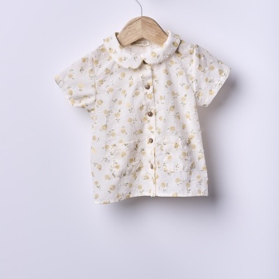 Camisa infantil branca com flores amarelas e botões de madeira pendurada num cabide