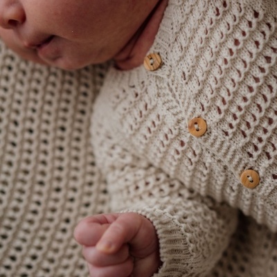Macacão de bebé em malha bege com botões de madeira.