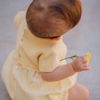 Bebé de costas com roupa amarela e flor na mão
