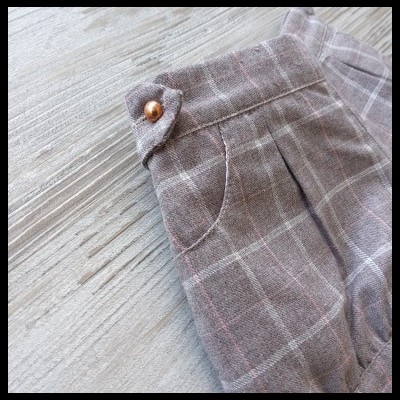 calças xadrez bege com botão cobre e bolsos sobre madeira clara