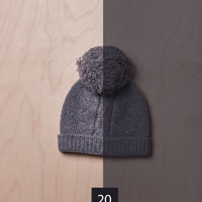 Gorro cinzento com pompom sobre fundo de madeira dividido em duas cores