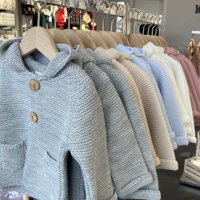 Casacos de malha infantil de várias cores pendurados numa estrutura metálica em loja