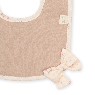 Babete rosa claro com acabamento creme e detalhe de laço, etiqueta com desenho de ave