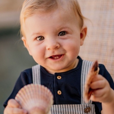 Bebé a segurar duas conchas marinhas sentado numa cadeira de tecido bege