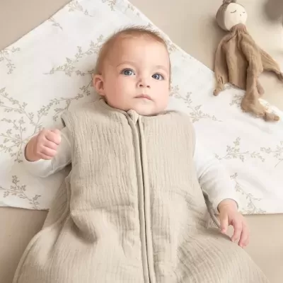 Bebé deitado com saco de dormir bege e manta com padrão floral