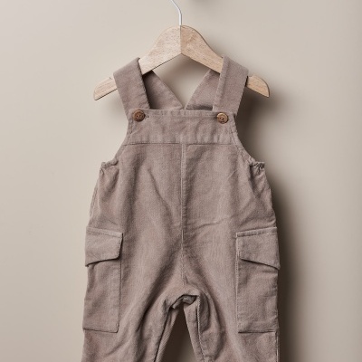 Macacão bege castanho em tecido veludo com botões de madeira, pendurado num cabide de madeira