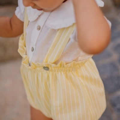 Roupa de criança com camisa branca e calção amarelo às riscas com suspensórios