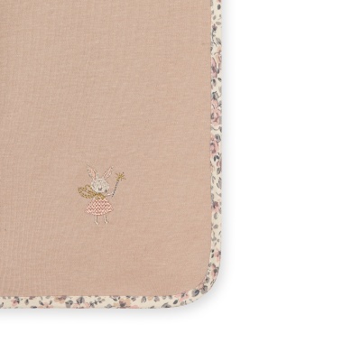 Detalhe de tecido bege com borda floral e bordado de coelho com vestido rosa.