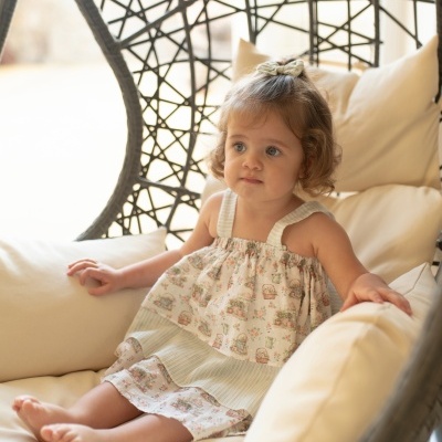 Cadeira suspensa de vime com almofadas creme e criança vestindo vestido branco