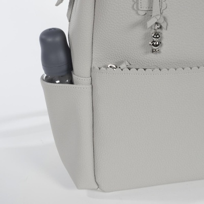 Bolsa cinzenta clara com frasco cinzento escuro no bolso lateral e pendente metálico decorativo.