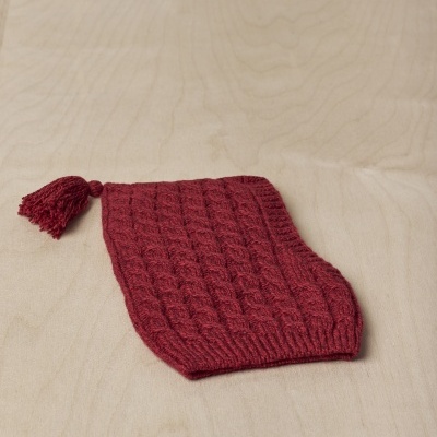 Capa vermelha em malha texturizada com pompom sobre madeira clara