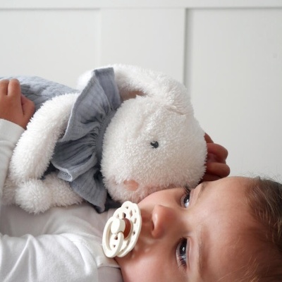 Criança deitada com chupeta e ursinho peluche