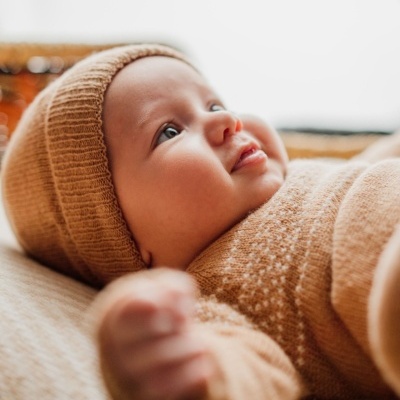 Bebé com roupa de malha cor de areia deitado num colchão macio