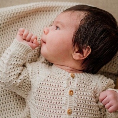 Bebé com camisola de malha bege e manta do mesmo tom.