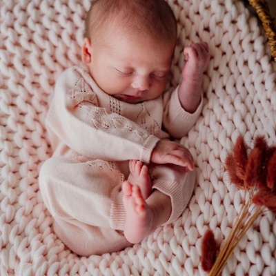 Bebé vestido com pijama de malha creme em cesta com manta de malha e flores secas.