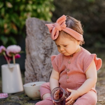 Criança com roupa rosa de malha sentada ao ar livre segurando frasco de vidro