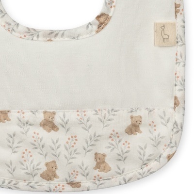 Babete branco com padrão de ursos e folhas e etiqueta com desenho de cadeira.