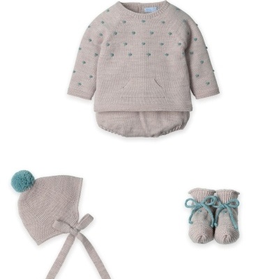 Conjunto de roupas para bebé em malha cinzenta com pontos azuis, gorro com pompom e botins com laços azuis.