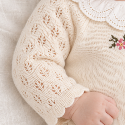 Roupa de bebé creme com gola bordada e padrão rendilhado nas mangas.