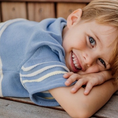Criança deitada sorridente com camisola azul clara de malha com riscas brancas