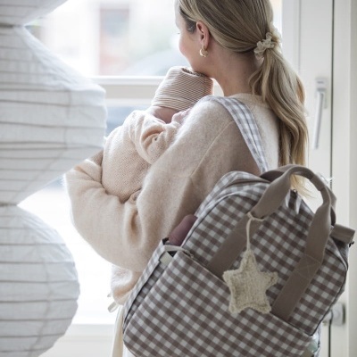 Mulher com mochila estampada segurando bebé junto a janela