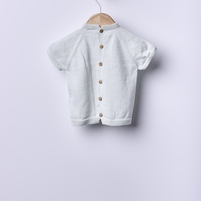 Camisola de malha branca para bebé com botões nas costas pendurada num cabide de madeira