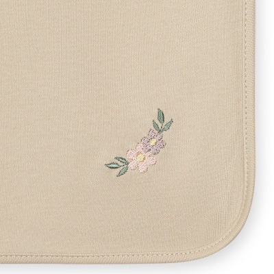 Toalha bege com bordado floral em tons pastel e borda costurada arredondada.