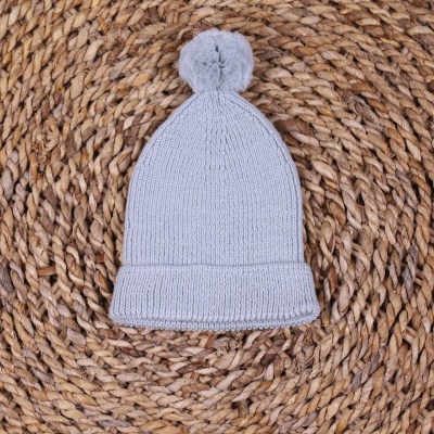 Gorro cinzento com pompom sobre superfície trançada