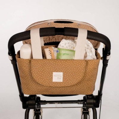 Organizador bege com pontos brancos preso a um carrinho de bebé com itens para bebé