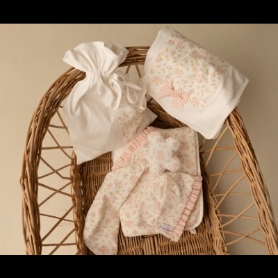 Conjunto de tecido floral rosa e branco com saco de cordão numa cadeira de vime