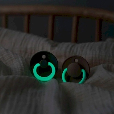 Duas chupetas com anel luminoso verde sobre tecido branco