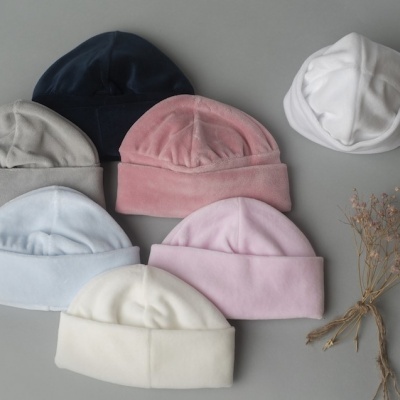 Sete gorros de bebés em tons neutros e pastel com ramo de flores secas ao lado