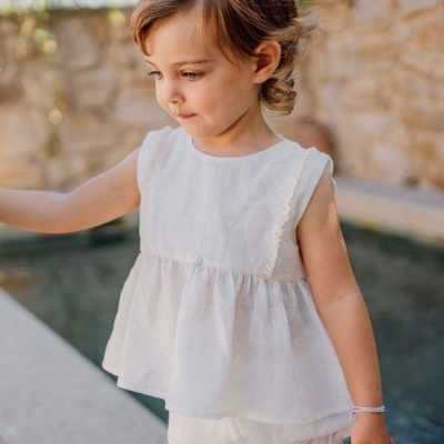 Criança de roupa branca leve junto a piscina com muro de pedra ao fundo