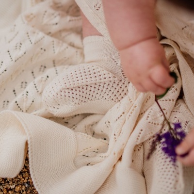 Meia e manta de malha bege claro com bebê segurando flor roxa sobre pedras