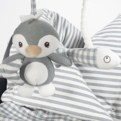Brinquedo de pelúcia pinguim pendurado em estrutura riscada e xadrez cinza e branco