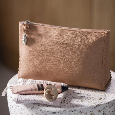 Necessaire bege texturizada com fecho e acessórios de cosmética sobre base redonda de pedra colorida.