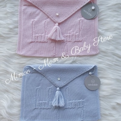 Dois envoltórios de malha para bebé, um rosa e outro azul, com botão e tassel, sobre fundo branco felpudo