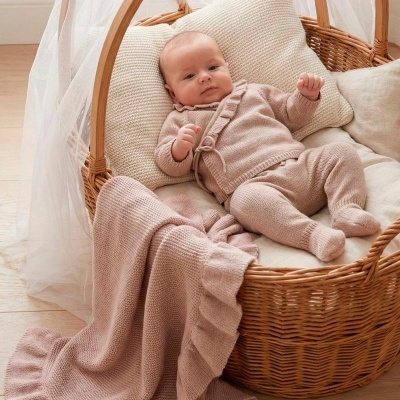 Bebé em cesto de verga com roupa e manta cor de rosa