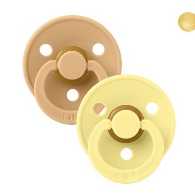 Duas chupetas de silicone, uma amarela e outra castanha clara, com orifícios circulares e anel frontal