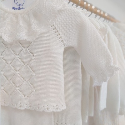 Roupas brancas de bebé em malha penduradas em cabides