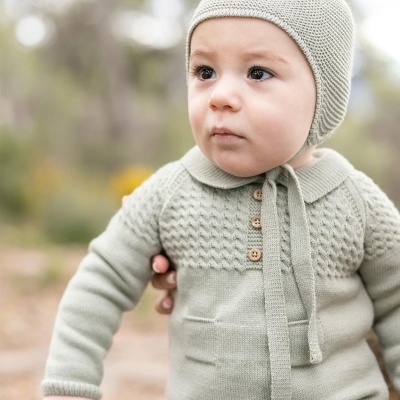 Bebé com fato de malha bege e gorro com pompom ao ar livre