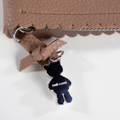 Detalhe de acessório de pele castanha com pendente metálico em forma de figura humana