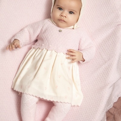 Bebé com roupa rosa e branca deitada sobre manta rosa
