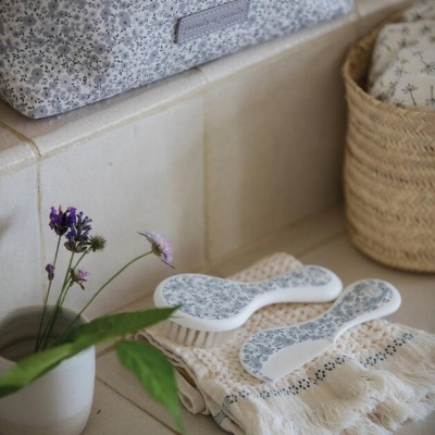 Duas escovas de cabelo florais sobre toalha bege com franjas e flores em pote branco