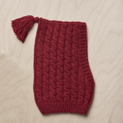 Meia vermelha com padrão de trança e pompom sobre superfície de madeira clara