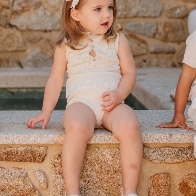 Criança vestida de branco com laço no cabelo a sentar-se numa parede de pedra