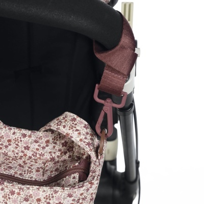 Detalhe de carrinho com pega preta, alça castanha e bolsa floral rosa e vermelha.
