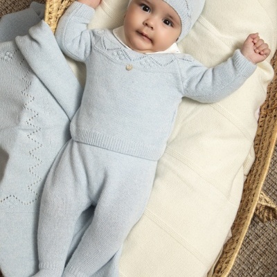Bebé deitado numa cesta com roupa azul clara e gorro com pompom.