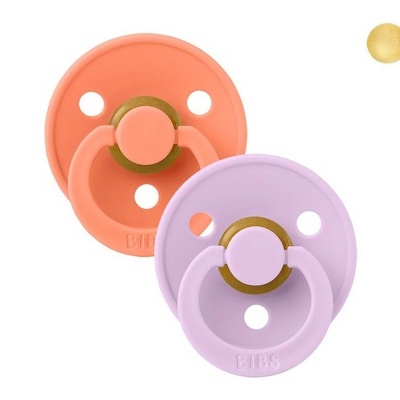 Dois chupetas BIBS cor de pêssego e lilás com orifícios num fundo branco