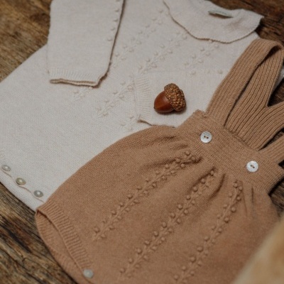Conjunto de roupa de bebé em malha castanho e creme sobre madeira